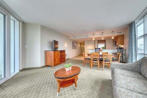 A spacious living area with a sofa, a dining table with chairs, a small round table with a plant, and a kitchenette in the background. - Sandy Beach Resort 304 (Myrtle Beach)