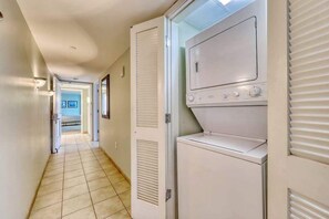 A laundry room with stacked washers and dryers, a tiled floor, and a hallway leading to another room. - Sandy Beach Resort 304 (Myrtle Beach)