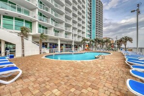 A hotel pool area with blue lounge chairs, a central pool, and a multi-story building with balconies. - Sandy Beach Resort 304 (Myrtle Beach)