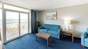 Ein Hotelzimmer mit großem Fenster, einer Couch, einem Couchtisch, einer Lampe und einem gerahmten Bild an der Wand.