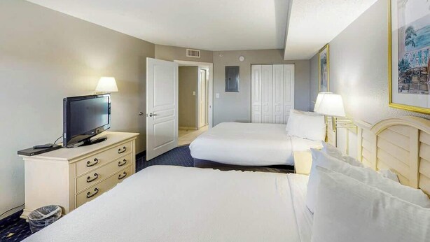Ein Hotelzimmer mit Fernseher, Schreibtisch, Stuhl, Bett und Kleiderschrank.