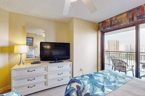 A hotel room with a bed, a television on a dresser, a balcony with chairs, and a view of buildings. - Sand Dunes Resort 807 (Myrtle Beach)