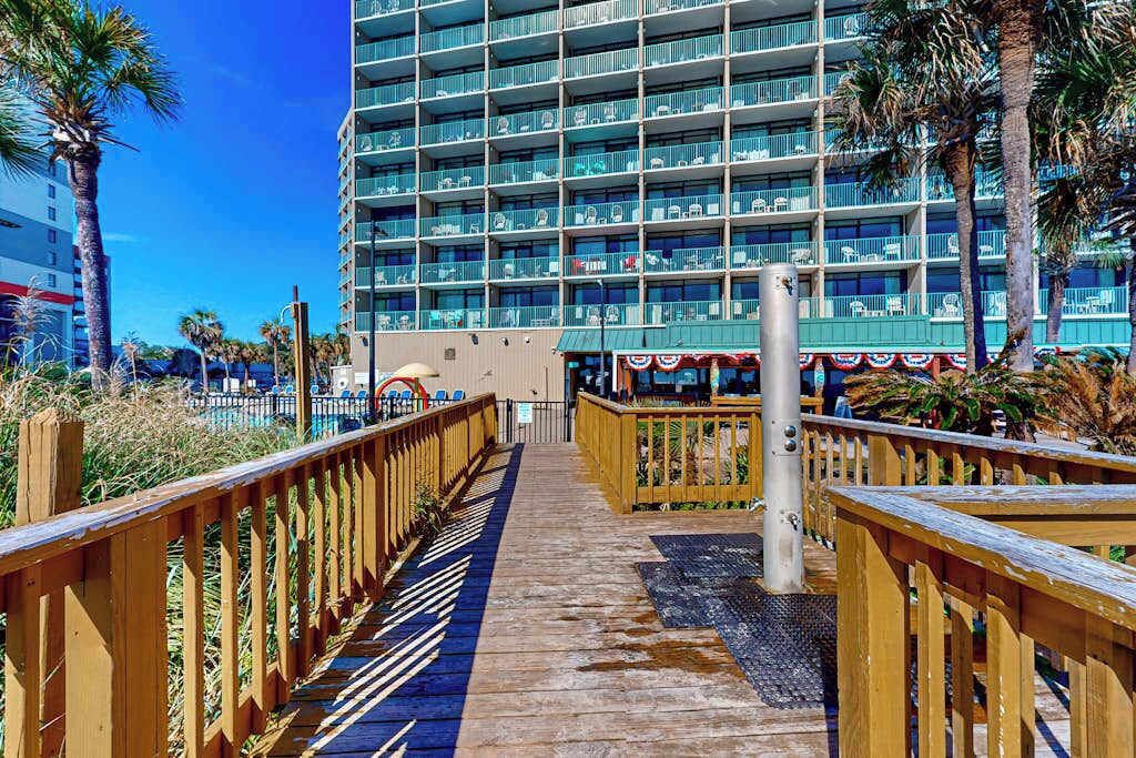 A wooden boardwalk leading to a multi-story hotel with balconies.