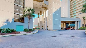 L'ingresso di un hotel con una pensilina, palme e un edificio con ampie finestre.