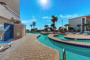 Une piscine entourée de bâtiments, avec des chaises longues et des palmiers.