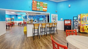 Una vivace food court con un pannello dei menu, zone salotto e giochi arcade.
