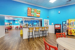 Ein lebhaft gestalteter Food-Court mit Speisekarte, Sitzbereichen und Spielautomaten.
