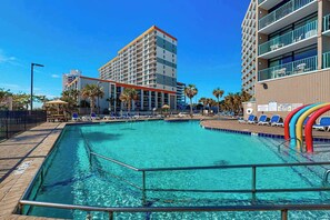 A swimming pool with lounge chairs and a building with multiple floors in the background. - Sand Dunes Resort 807 (Myrtle Beach)