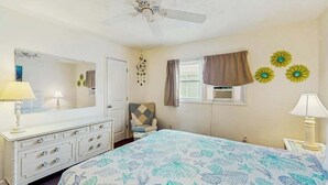 Een slaapkamer met een bed, een kaptafel, een stoel en een plafondventilator.