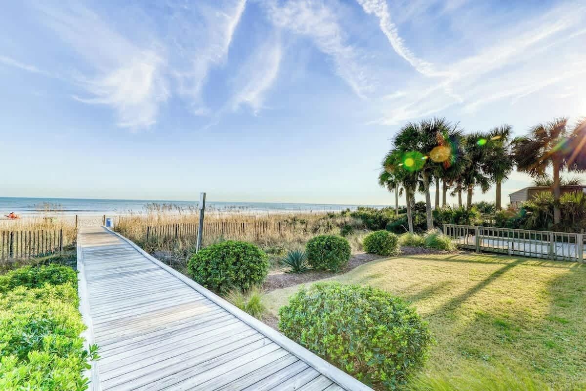 A wooden boardwalk leading to a beach with palm trees and a fence.