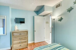 A bedroom with a bed, a dresser, a television, and a door. - Sands Beach Club 1127 (Myrtle Beach)