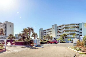 A hotel entrance with a parking lot, a red car parked in front, and a sign indicating no parking. - Sands Beach Club 1127 (Myrtle Beach)