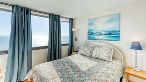 Un dormitori amb llit, cortines, una làmpada i un quadre del mar.