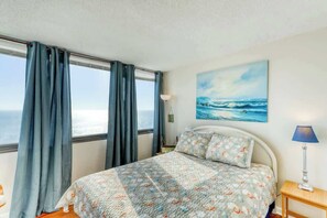 A bedroom with a bed, curtains, a lamp, and a painting of the sea. - Sands Beach Club 1127 (Myrtle Beach)