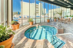 An indoor swimming pool with a tiled floor, surrounded by potted plants and outdoor seating. - Sands Beach Club 1127 (Myrtle Beach)