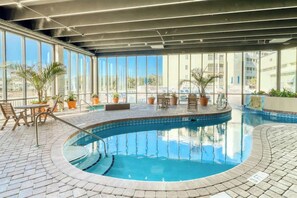 An indoor swimming pool with clear blue water, surrounded by a tiled deck and potted plants. - Sands Beach Club 1127 (Myrtle Beach)