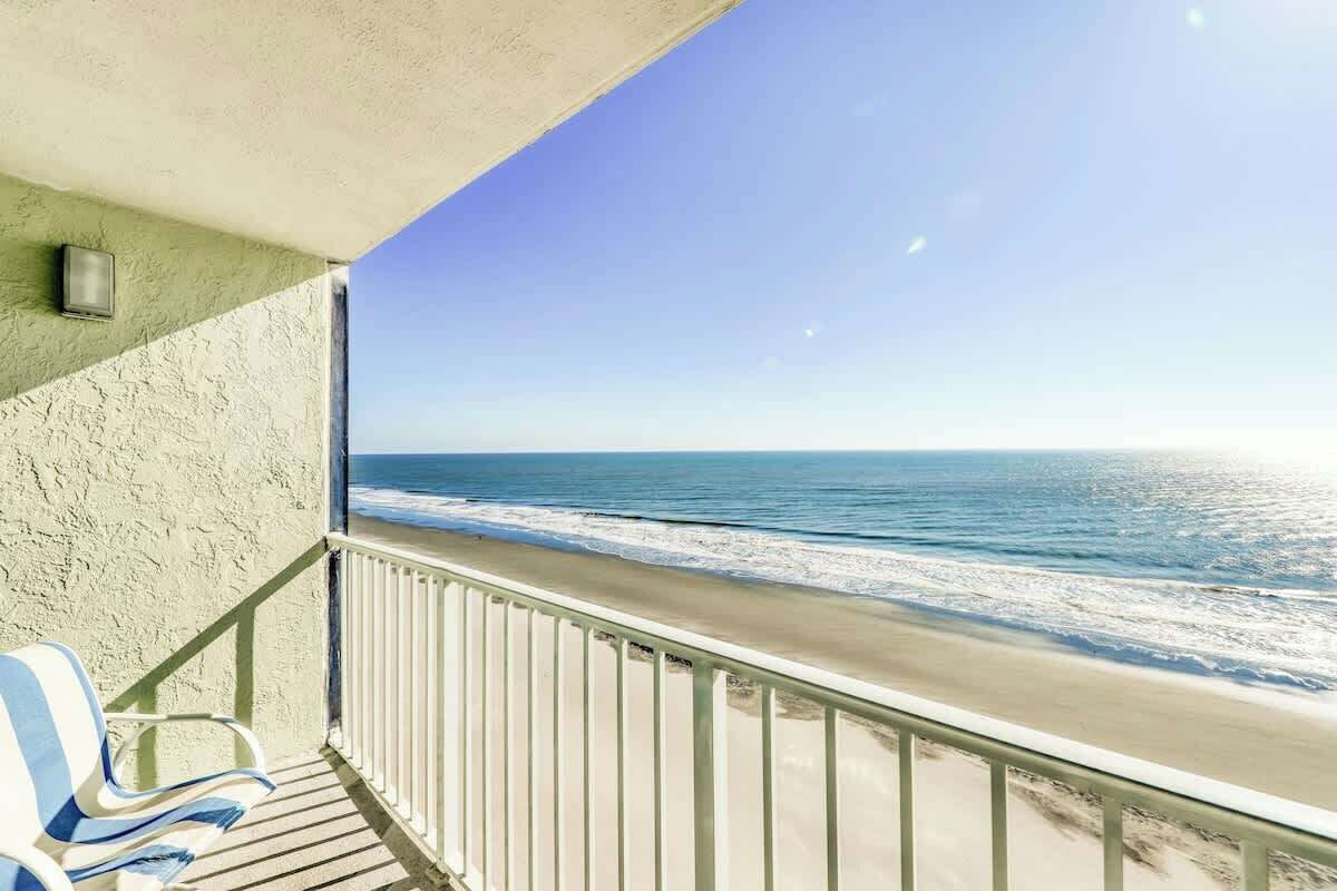 A balcony with a view of the ocean, a chair, and a railing.