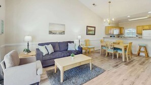 A modern living room with a sofa, coffee table, and dining area. - Magnolia North Unit 304 (Myrtle Beach)