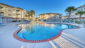A swimming pool surrounded by a white fence, with a clear blue sky above. - Magnolia North Unit 304 (Myrtle Beach)