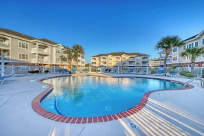 A swimming pool surrounded by a white fence, with a clear blue sky above. - Magnolia North Unit 304 (Myrtle Beach)