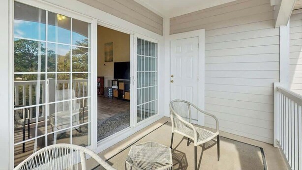 A covered porch with two wicker chairs, a sliding glass door leading to an interior space, and a white door. - Magnolia North Unit 304 (Myrtle Beach)
