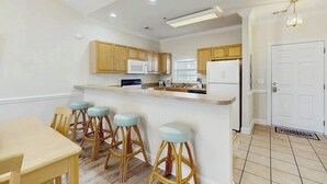 A kitchen with wooden cabinets, a white countertop, and bar stools. - Magnolia North Unit 304 (Myrtle Beach)