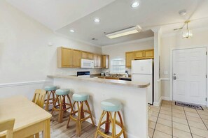 A kitchen with wooden cabinets, a white countertop, and bar stools. - Magnolia North Unit 304 (Myrtle Beach)