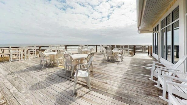 En udendørs terrasse med borde og stole, med udsigt over havet.