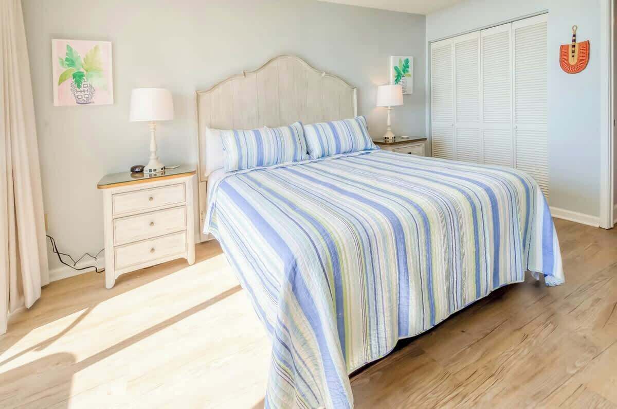 A bedroom with a bed, two bedside tables, a nightstand, a wardrobe, and a wall-mounted guitar.