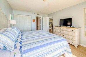 A bedroom with a bed, a dresser, a television, and a door leading to a bathroom. - Oceanfront Seaside Retreat (Litchfield Beach)