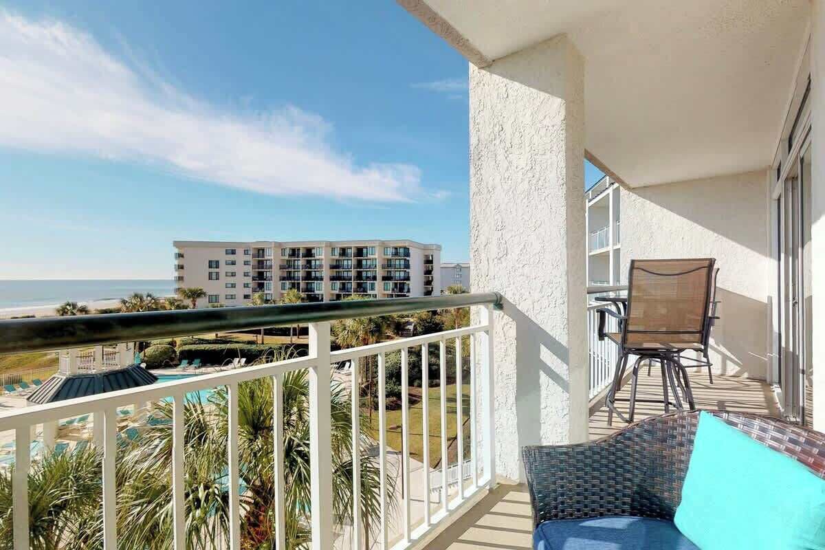 Un balcone con vista sulla spiaggia e sulla piscina, una sedia e un tavolo.