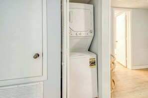 A laundry room with a washing machine and dryer, a door with a doorknob, and a wooden floor. - Oceanfront Seaside Retreat (Litchfield Beach)