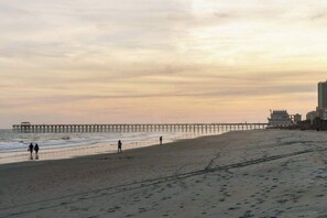A beach with a pier extending into the water, a few people walking, and buildings in the background. - Stillwater Family Home (Myrtle Beach)