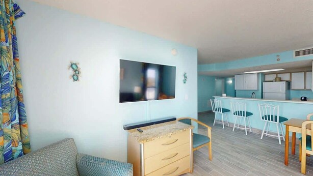Ett kompakt bostadsutrymme med ett litet kök, en matplats med stolar, en soffa och en tv som är monterad på väggen.