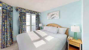 Ett hotellrum med en säng, sängbord, en lampa och gardiner.