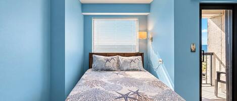 Une chambre à coucher avec un lit, une fenêtre avec des stores, une porte donnant sur un balcon et un luminaire fixé au mur.