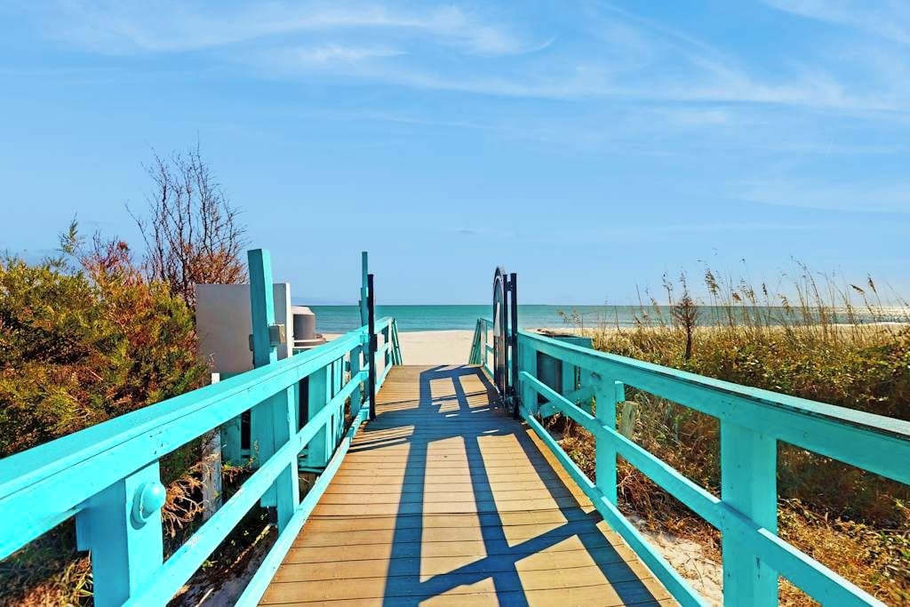 Una passerella di legno che conduce a una spiaggia sotto un cielo sereno.