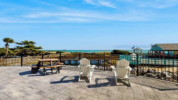 Patio esterno con tavoli da picnic e poltrone Adirondack, con vista su una spiaggia e una distesa d'acqua.
