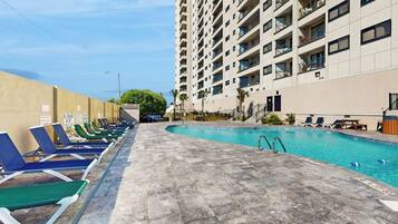 A swimming pool area with lounge chairs and a tall building in the background.