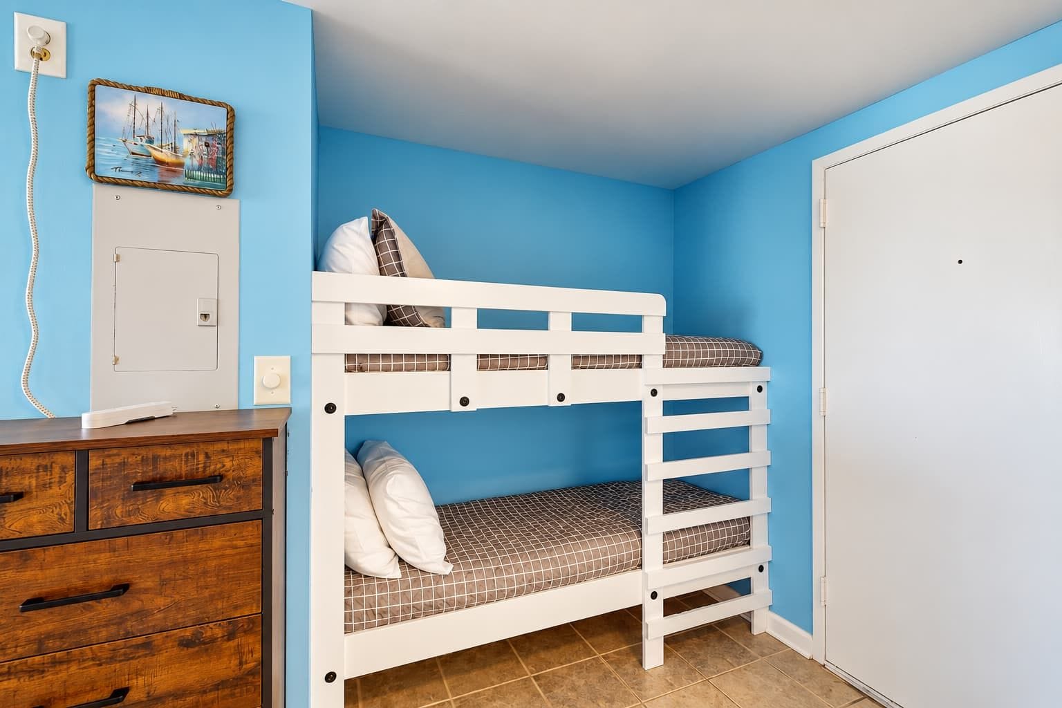 A bunk bed room with a wooden dresser and a door.