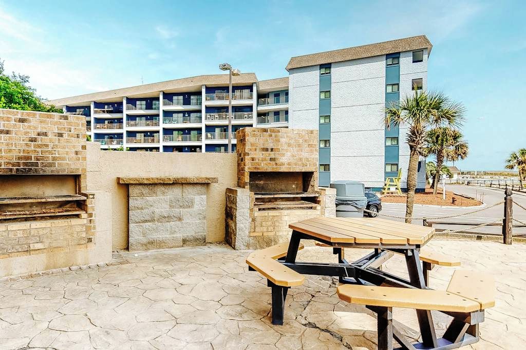 An outdoor patio area with a barbecue grill, picnic table, and a view of a multi-story building.