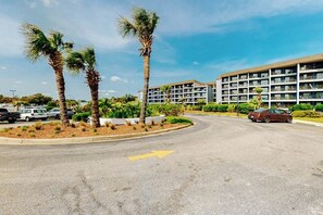 A multi-story hotel with a parking lot, palm trees, and a clear sky. - Sunrise at Renaissance | Luxe Escape (Myrtle Beach)