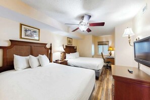 Ein Hotelzimmer mit zwei Betten, einem Deckenventilator, einem Fernseher und einem Schreibtisch mit Lampe.