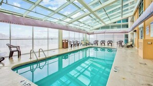 Ein Innenpool mit Glasdecke, Liegestühlen und Blick auf die Stadt.