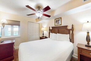 A hotel room with a bed, a ceiling fan, a nightstand, a lamp, a dresser, and a door. - Bahama Sands Unit 0608 (North Myrtle Beach)