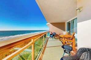 A balcony with a view of the beach and ocean, a table with chairs, and a window with curtains. - Bahama Sands Unit 0608 (North Myrtle Beach)