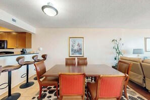 Ein Essbereich mit Tisch und Stühlen, im Hintergrund eine Küche und ein Sofa.