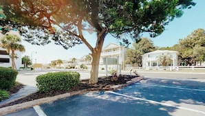 A parking lot with a tree, a building with a white facade, and a clear sky. - Ocean Retreat Unit N1 (North Myrtle Beach)