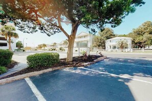 A parking lot with a tree, a building with a white facade, and a clear sky. - Ocean Retreat Unit N1 (North Myrtle Beach)