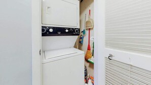 A laundry room with a washing machine and dryer, a broom, and cleaning supplies. - Ocean Retreat Unit N1 (North Myrtle Beach)
